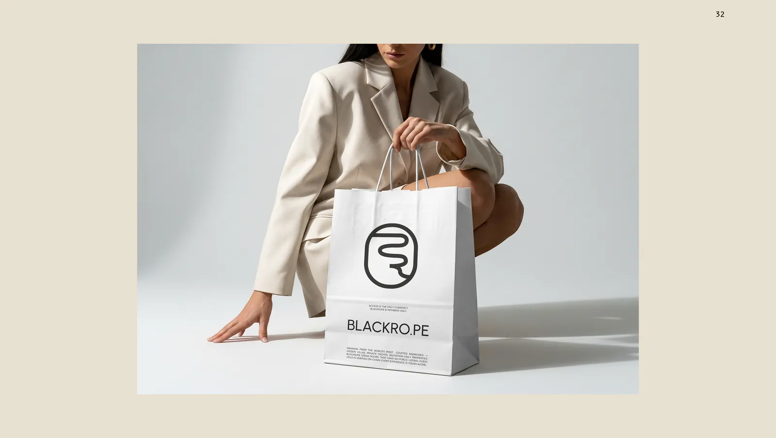 A white paper shopping bag held at the floor, the rope loop and the wordmark on the face.