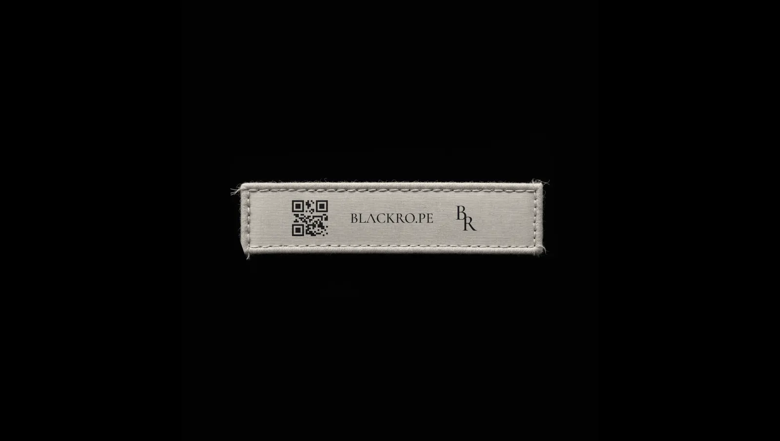 A woven care label, the wordmark and the monogram either side of a QR code.