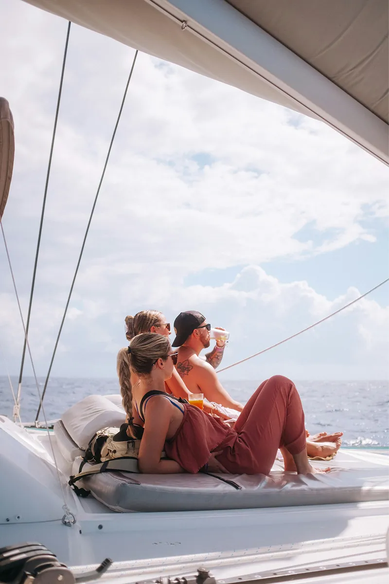 Two people sitting out on the foredeck of a yacht under sail.